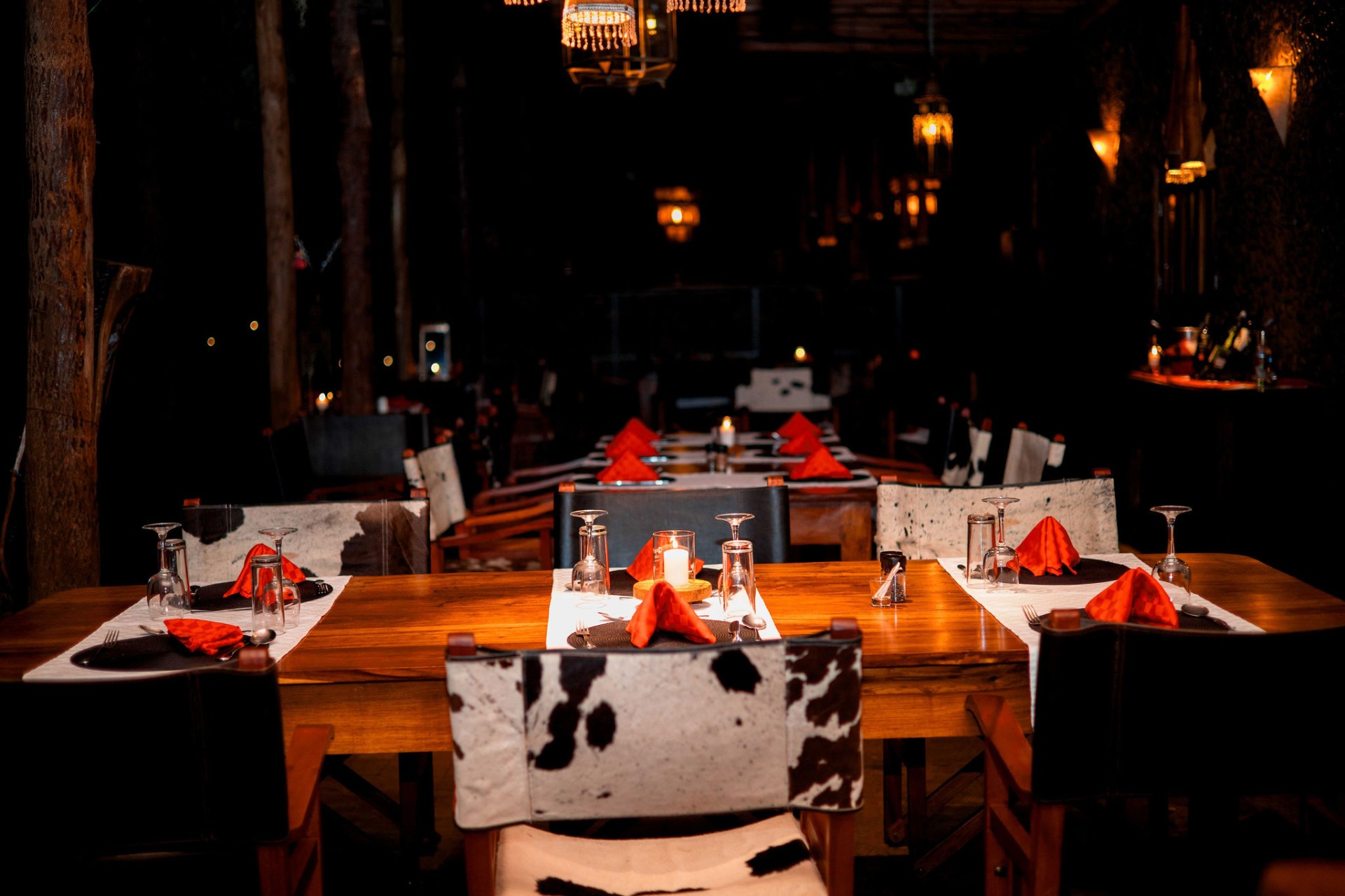 Candlelit dining hall at Mtoni River Lodge with cowhide chairs and lantern light