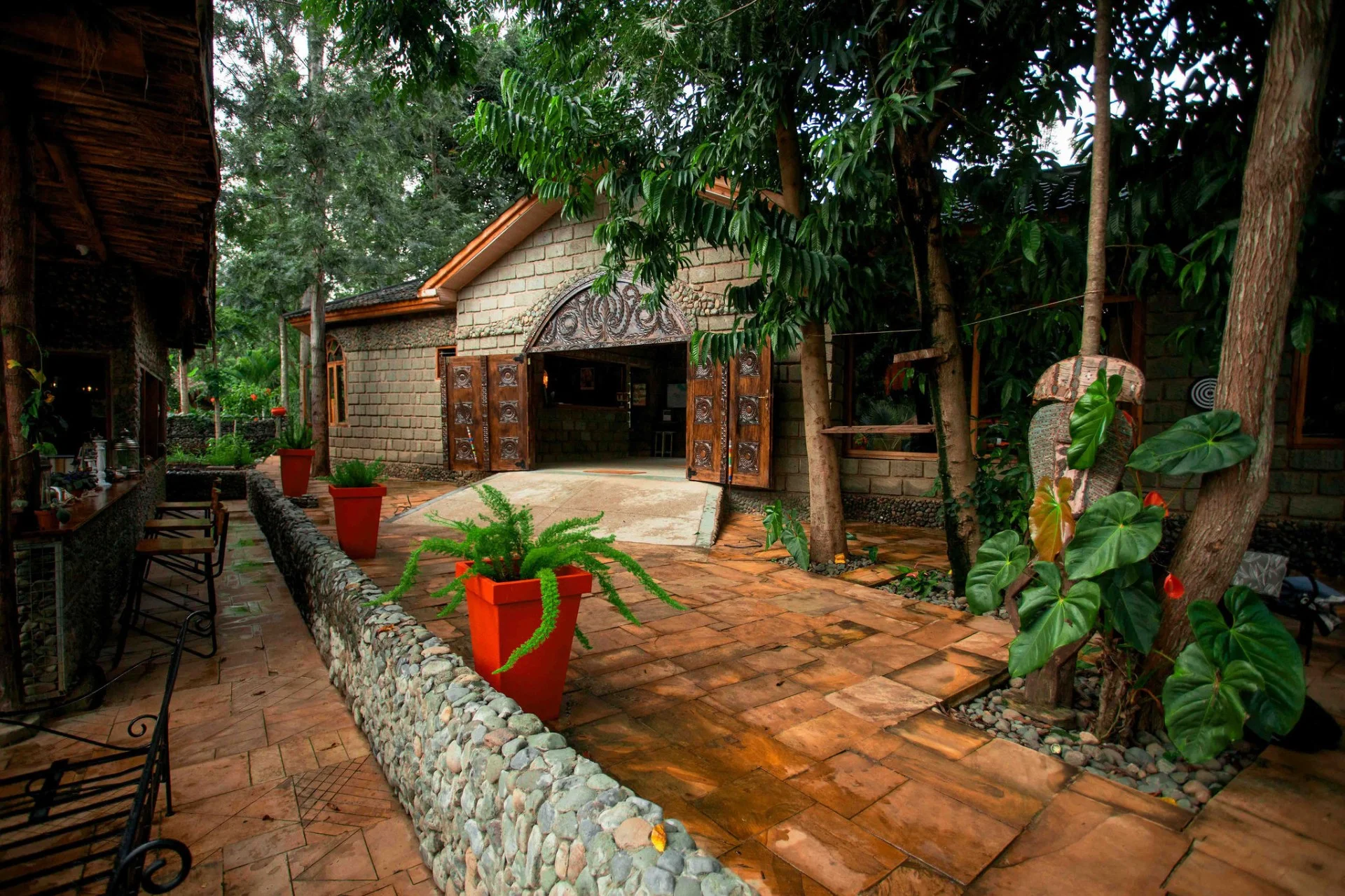 Stone entrance to Mtoni River Lodge with carved wooden doors, surrounded by tropical garden
