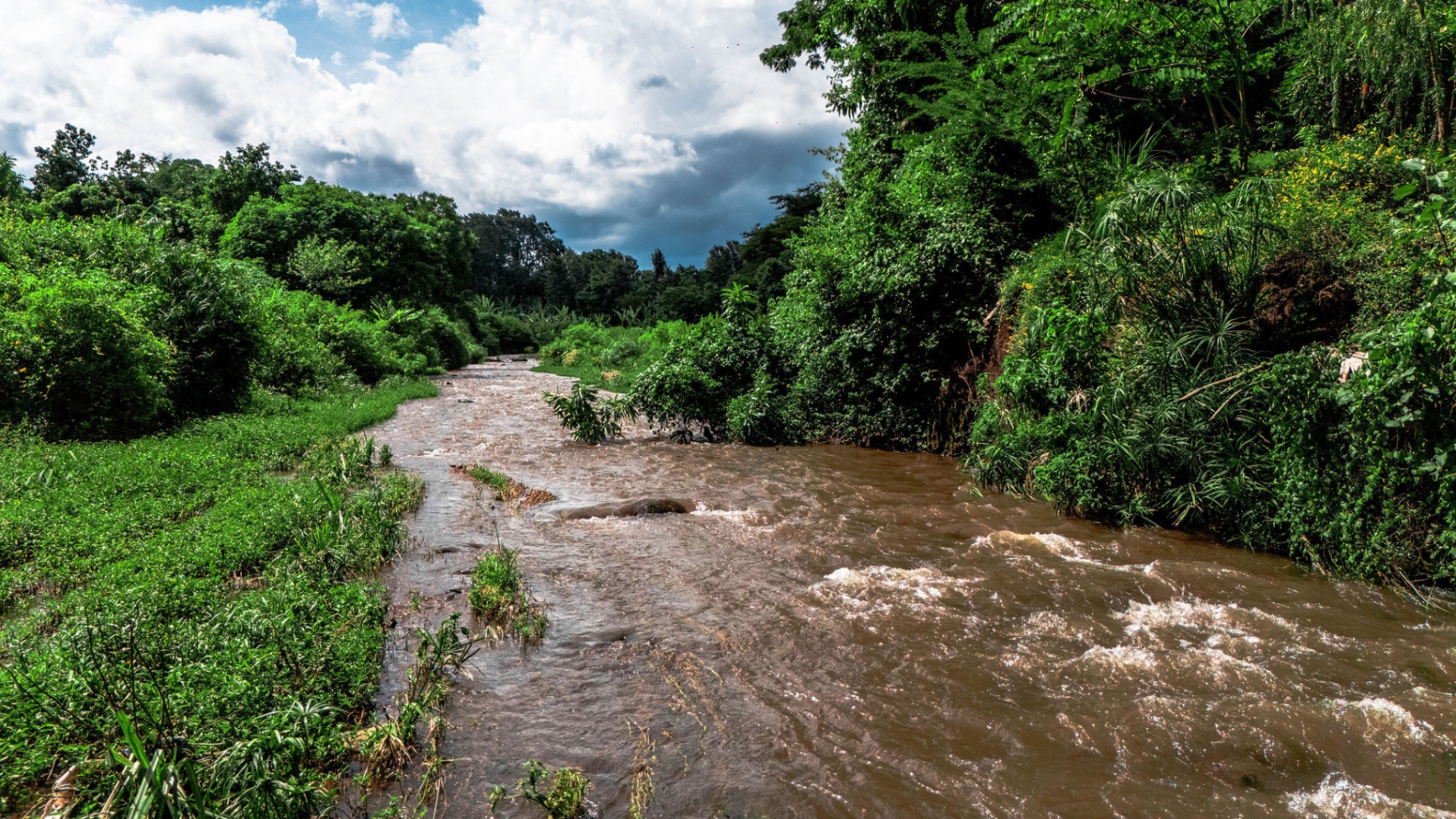 The Nduruma River in full flow, framed by lush green banks under a dramatic sky